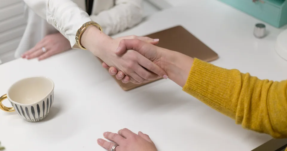 Two people shaking hands across a desk
